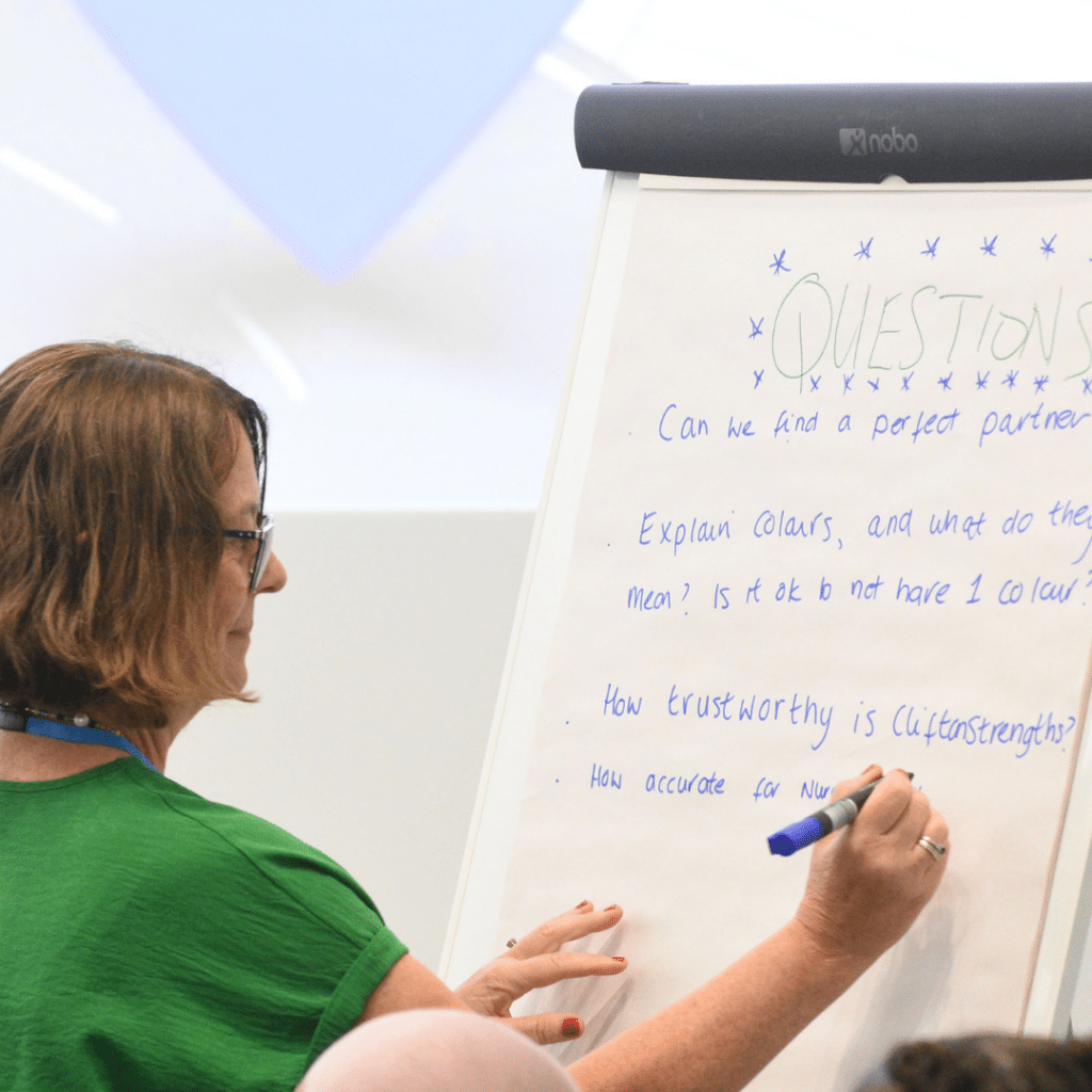 Lady in green with dark hair writing on a flip chart.